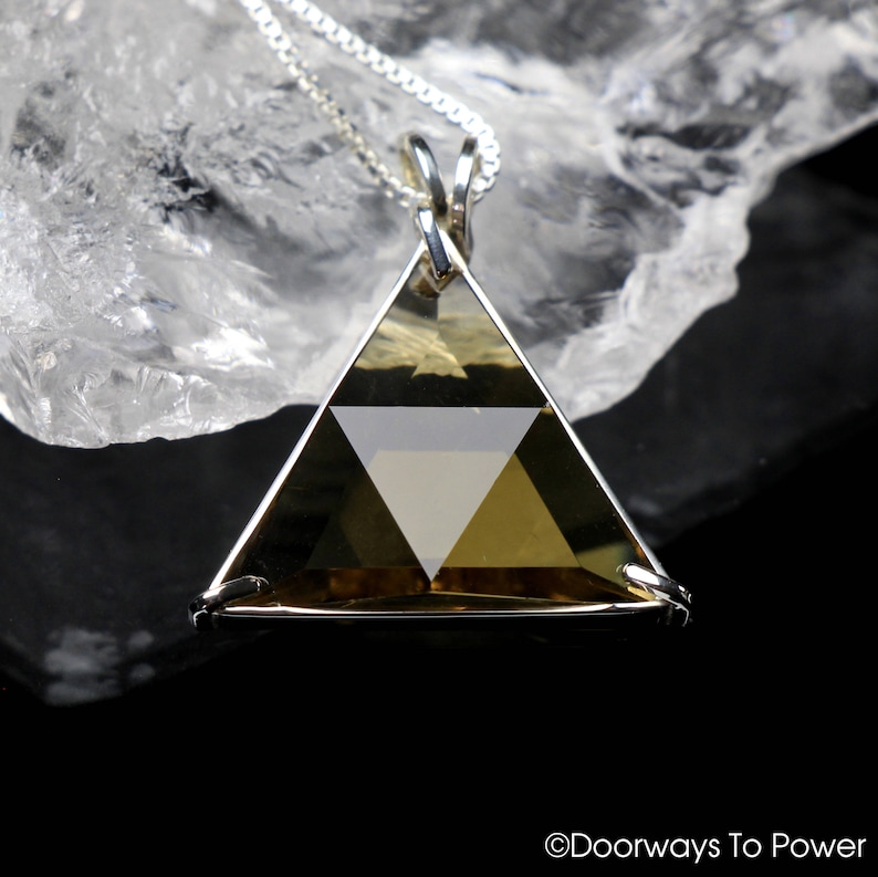 May include: A silver chain necklace with a gold-toned triangular pendant featuring a geometric design. The pendant is made of faceted crystal.