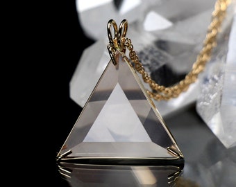 May include: A clear quartz crystal pendant in the shape of a Star of David, with a gold-toned chain. The pendant is hanging from a white crystal cluster.