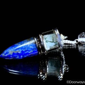 May include: A pendulum with a blue lapis lazuli point and a silver-colored metal casing. The pendulum has a clear glass section with a light blue stone inside. A small, clear crystal ball hangs from a chain.