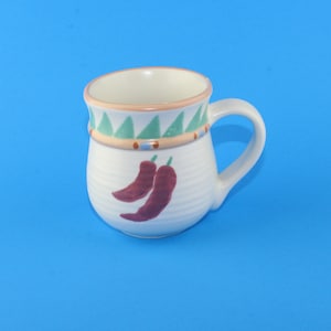 Può includere: Tazza in ceramica bianca con una fascia decorata di verde, marrone e blu intorno alla parte superiore. La tazza ha un manico e presenta un design a peperoncino rosso.