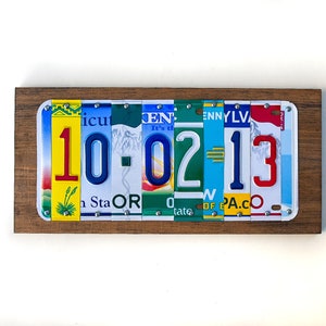 Puede incluir: Una placa de madera con la fecha 10-02-13 escrita con placas de matr&iacute;cula de diferentes estados. Los n&uacute;meros son rojos, azules y amarillos.