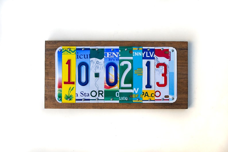 Puede incluir: Una placa de madera con la fecha 10-02-13 escrita con placas de matr&iacute;cula de diferentes estados. Los n&uacute;meros son rojos, azules y amarillos.