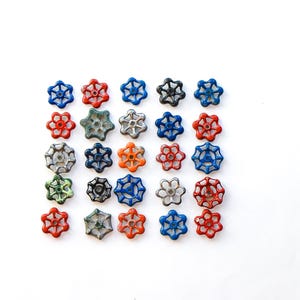 May include: A collection of colorful, vintage-style valve handles arranged on a white surface. The handles are in various colors, including red, blue, orange, green, and silver, with a star-shaped design. These could be used for industrial decor.