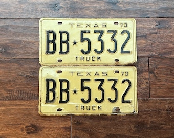 May include: Two vintage yellow Texas license plates with black lettering. The plates read "TEXAS 73" and "BB*5332 TRUCK".