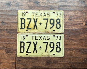 May include: Two vintage Texas license plates with the same number, "BZX 798", and the year "73" printed on them. The plates are yellow with black lettering and a star between the letters and numbers.