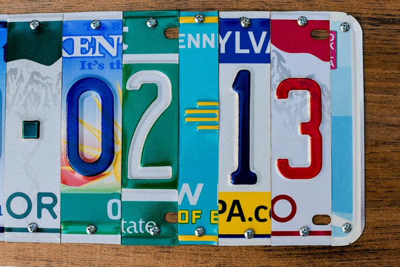 Puede incluir: Un primer plano de una obra de arte de pared hecha con placas de matr&iacute;cula. Las placas de matr&iacute;cula est&aacute;n dispuestas para deletrear el n&uacute;mero "0213". Las placas de matr&iacute;cula son de diferentes estados, incluyendo Pensilvania y Oklahoma.