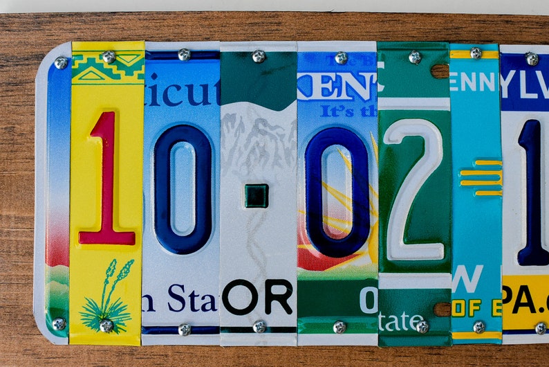 Puede incluir: Una pieza de arte de pared hecha con placas de matr&iacute;cula reutilizadas, que presenta los n&uacute;meros 10-02-1, con un esquema de color amarillo, rojo, azul, verde y turquesa.