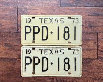 May include: Two vintage Texas license plates with the same number, "PPD 181", on a brown wooden background.