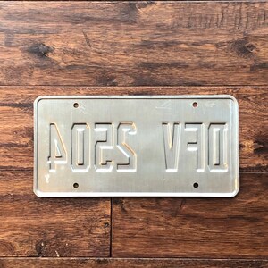 Op de afbeelding: Een zilveren metalen kentekenplaat met de tekst "D1F V5204" in zwarte letters.