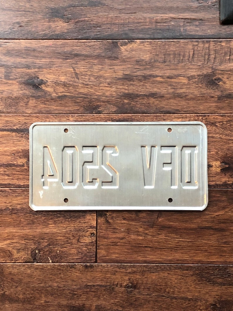 Op de afbeelding: Een zilveren metalen kentekenplaat met de tekst "D1F V5204" in zwarte letters.