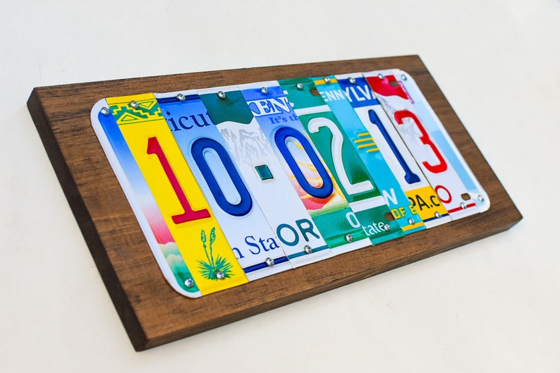 Puede incluir: Una placa de madera con la fecha 10-02-13 escrita con placas de matr&iacute;cula de diferentes estados. Los n&uacute;meros son rojos, azules y verdes. La placa es una excelente manera de conmemorar una fecha especial.