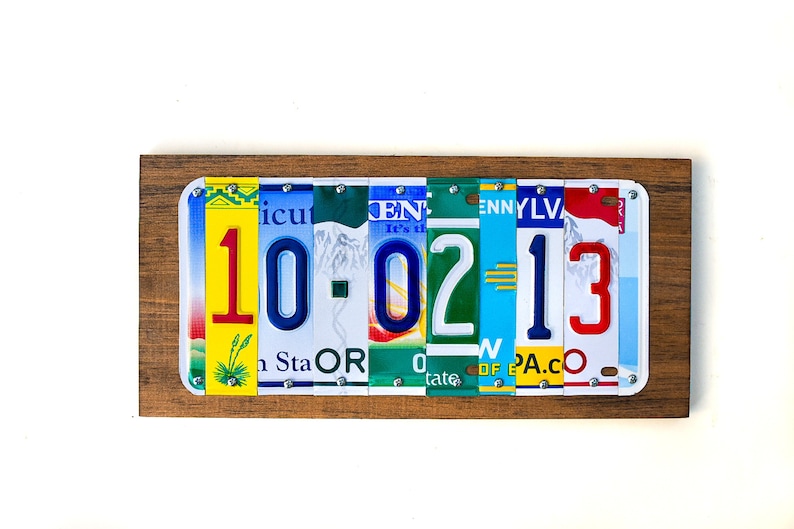 Puede incluir: Una placa de madera con la fecha 10-02-13 escrita con placas de matr&iacute;cula de colores. La placa es de madera y tiene un aspecto r&uacute;stico.