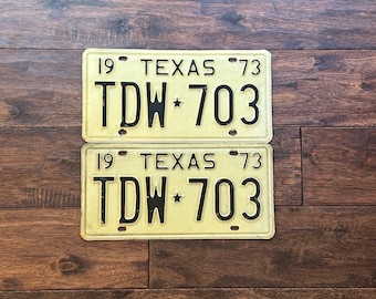 May include: Two vintage yellow Texas license plates with black lettering. The plates read "19 TEXAS 73" and "TDW 703".