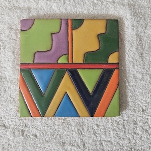 May include: A square ceramic tile with a geometric pattern in shades of green, yellow, orange, blue, purple, and black.