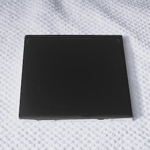 May include: A black square tile with a smooth, glossy surface.