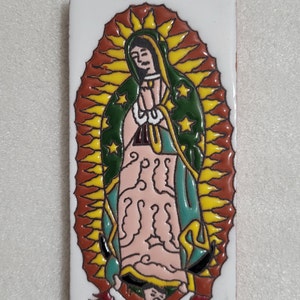 May include: A ceramic tile with a colorful image of the Virgin Mary. The image is surrounded by a yellow halo with stars and a red and yellow background.