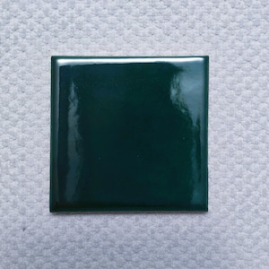 May include: A square, dark green ceramic tile with a glossy finish.