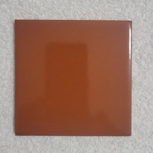 May include: A square, terracotta-colored ceramic tile with a glossy finish.