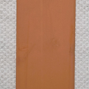 May include: A rectangular terracotta tile with a smooth, matte finish and a uniform reddish-brown color. The tile features clean, straight edges and a flat surface, presenting a simple and functional design suitable for various construction or decorative projects.