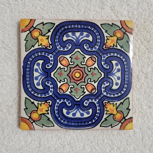 May include: A square ceramic tile with a blue, green, yellow, and red geometric pattern. The tile has a white background and features a central floral design.