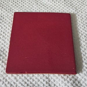 May include: A solid red square tile. The tile is smooth and has a slightly glossy finish.