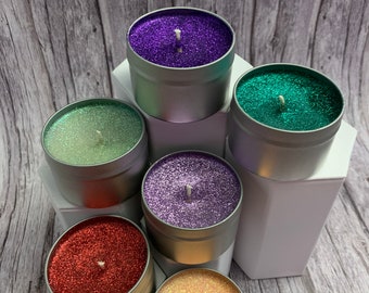 May include: Six small candles in silver tins with glitter on top. The candles are in the colors purple, green, light green, lavender, red, and peach.