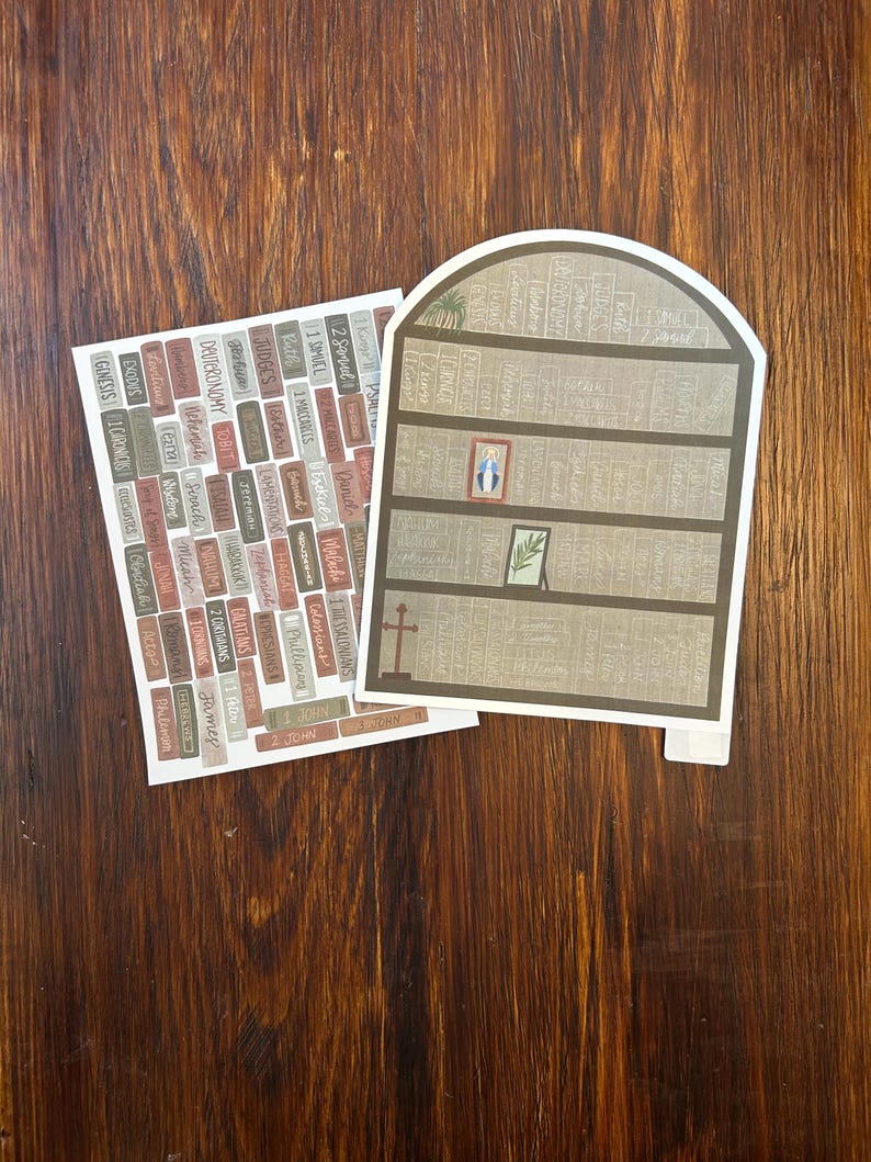K&ouml;nnte beinhalten: Zwei Papierausstiche auf einer Holzoberfl&auml;che. Einer ist ein B&uuml;cherregal-Design mit einem Kreuz und gerahmter Kunst. Der andere ist eine Sammlung rechteckiger Etiketten mit Text. Die Etiketten tragen Namen wie "Genesis", "Exodus" und "Johannes".