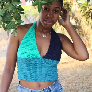 May include: A color-blocked halter top featuring a bright turquoise upper right section, a dark navy blue upper left section, and a solid teal lower section. The garment is constructed with a textured crochet stitch pattern and a deep V-neckline.