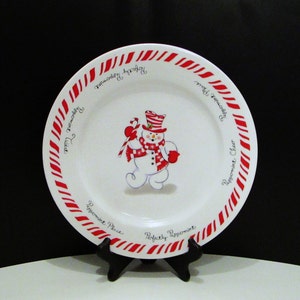 May include: White ceramic plate with a red and white candy cane border. The plate features a snowman illustration holding a candy cane. Text around the rim reads "Peppermint Twist", "Peppermint Place", "Peppermint Cheer", and "Perfectly Peppermint".