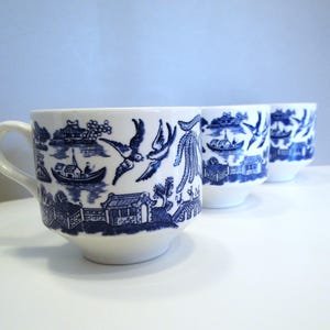May include: Three white ceramic mugs with blue illustrations. The mugs feature a classic blue and white design with scenes of boats, birds, and buildings. The mugs have a handle and a rounded shape.