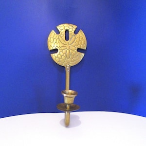 Peut inclure: Un bougeoir en laiton avec un motif d'étoile de mer. Le support présente un dessus circulaire avec un motif découpé et un motif floral central. La tige mène à un support en forme de coupe et à une petite base ronde. Le tout est sur fond bleu.