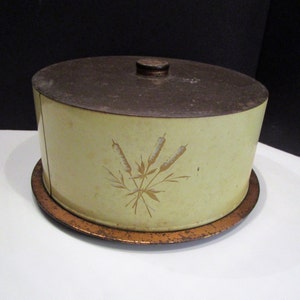 May include: Vintage yellow and brown metal cake carrier with a lid and a round base. The carrier features a decorative floral design in gold. The lid has a small, round handle. The base is a darker brown color.