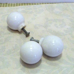Peut inclure: Trois boutons de meuble en céramique blanche avec une finition brillante. Chaque bouton a une forme ronde et est fixé à une vis métallique. Les boutons sont conçus pour les meubles et la décoration intérieure.
