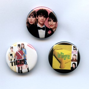 May include: Three round pinback buttons with colorful graphics. One button features a group of people, another has a band of people with the word "TIGRE" in large letters, and the third has the word "le Tigre" and images of people.