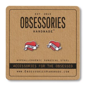 K&ouml;nnte beinhalten: Ohrstecker mit rotem Herzdesign und "MOM"-Banner. Auf einer braunen Karte mit dem Text "OBSESSORIES HANDMADE" und "ACCESSORIES FOR THE OBSESSED" pr&auml;sentiert.