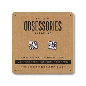 Op de afbeelding: Vierkante oorstekers met de tekst "MEAN PEOPLE SUCK" op een bruine kaart. De kaart toont "OBSESSORIES HANDMADE" en "ACCESSORIES FOR THE OBSESSED".
