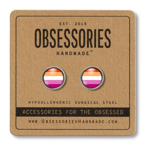 May include: A pair of round stud earrings featuring the lesbian pride flag design, set against a silver metal frame. The earrings are displayed on a brown card with the text "OBSESSORIES HANDMADE" and "ACCESSORIES FOR THE OBSESSED".