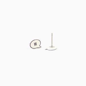 May include: A white speech bubble-shaped push pin with the word "HI" in black lettering. Next to it is a silver push pin with a white base. Both items are on a white background.