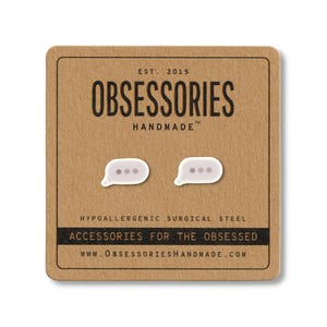 May include: A pair of white and gray message bubble earrings on a brown card. The card reads "OBSESSORIES HANDMADE" and "ACCESSORIES FOR THE OBSESSED". The earrings are made of hypoallergenic surgical steel.