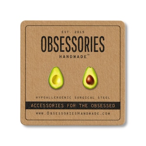 May include: A pair of avocado-shaped stud earrings on a brown card. The card reads "OBSESSORIES HANDMADE" and "ACCESSORIES FOR THE OBSESSED". The earrings are green with a yellow center and a brown pit. The card also says "HYPOALLERGENIC SURGICAL STEEL".