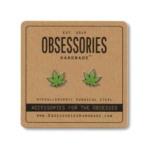 May include: A pair of green leaf-shaped stud earrings on a brown card. The card reads "OBSESSORIES HANDMADE" and "ACCESSORIES FOR THE OBSESSED". The earrings are made of hypoallergenic surgical steel.
