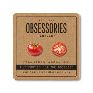 Könnte beinhalten: Eine quadratische, braune Karte mit dem Text "OBSESSORIES HANDMADE" und "EST. 2015". Die Karte zeigt eine ganze rote Tomate und eine Tomatenscheibe. Der Text "ACCESSORIES FOR THE OBSESSED" und "HYPOALLERGENIC SURGICAL STEEL" sind ebenfalls sichtbar.
