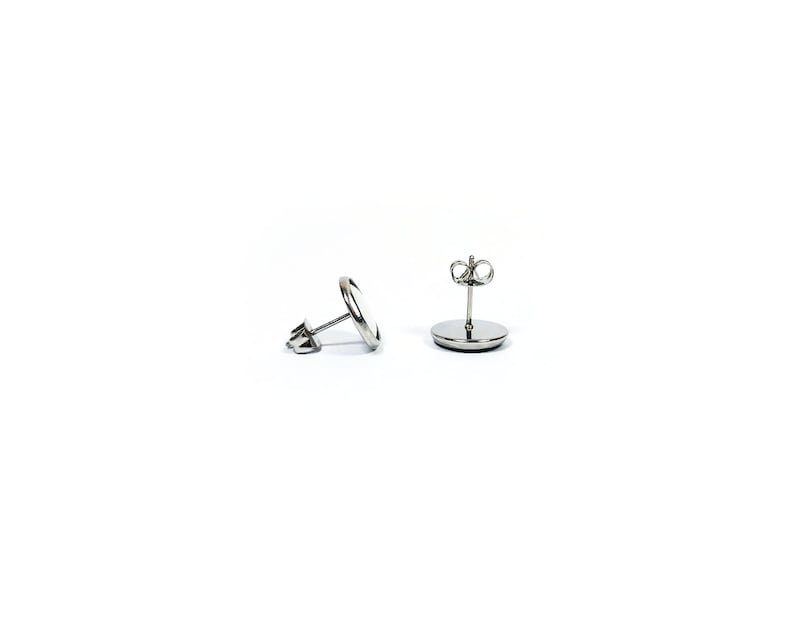 May include: A pair of silver stud earrings with a round, flat design. The earrings have a post and butterfly backing.
