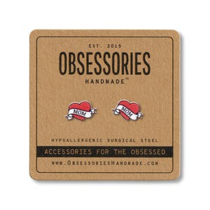 K&ouml;nnte beinhalten: Rote herzf&ouml;rmige Ohrstecker mit "MOM"-Banner auf einer braunen Karte. Die Karte tr&auml;gt den Text "OBSESSORIES HANDMADE" und "ACCESSORIES FOR THE OBSESSED".