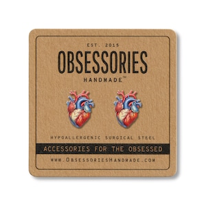 May include: A pair of anatomical heart stud earrings on a brown card. The earrings are red, blue, and white. The card has the text "OBSESSORIES HANDMADE" and "ACCESSORIES FOR THE OBSESSED".