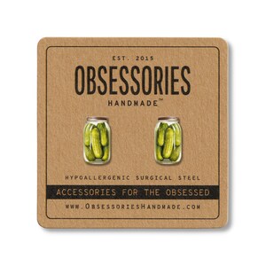 May include: A pair of pickle jar earrings on a brown card. The card has the text "OBSESSORIES HANDMADE" and "ACCESSORIES FOR THE OBSESSED". The earrings are made of hypoallergenic surgical steel.