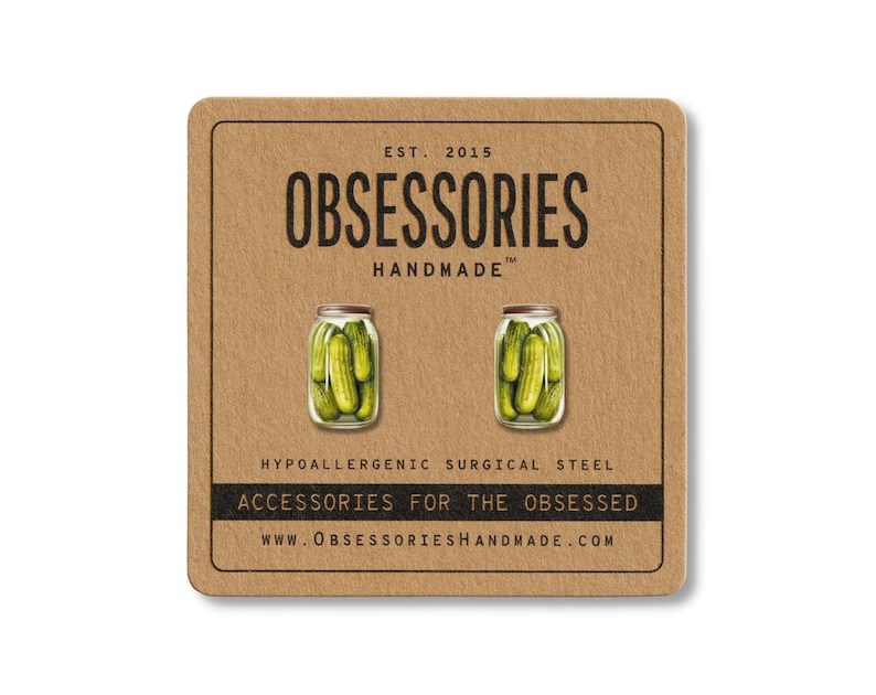 May include: A pair of pickle jar earrings on a brown card. The card has the text "OBSESSORIES HANDMADE" and "ACCESSORIES FOR THE OBSESSED". The earrings are made of hypoallergenic surgical steel.