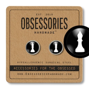Puede incluir: Un par de gemelos de pieza de ajedrez en blanco y negro con un alfil blanco. Los gemelos están hechos de acero quirúrgico hipoalergénico. El embalaje es marrón con el texto "OBSESSORIES HANDMADE" y "ACCESSORIES FOR THE OBSESSED".