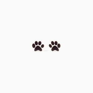 May include: A pair of small, dark paw print earrings. The earrings are black and have a simple, minimalist design. The paw prints are a popular symbol for pet lovers.