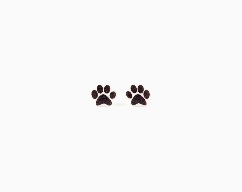 May include: A pair of small, dark paw print earrings. The earrings are black and have a simple, minimalist design. The paw prints are a popular symbol for pet lovers.